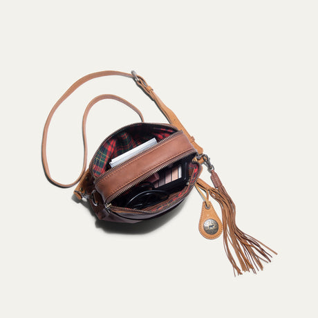 Top-down view of the cognac leather crossbody bag unzipped, showing a phone charging cable and makeup palette inside with plaid fabric lining