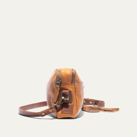 Side view of the tan leather crossbody bag showing the adjustable strap, zipper pulls, and fringe tassel