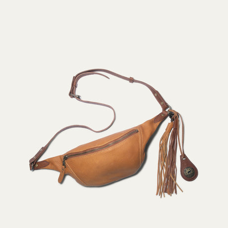 Will Leather Goods tan and cognac two-tone leather fanny pack with fringe tassel charm, flat lay with adjustable strap