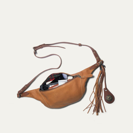 Tan and cognac leather fanny pack unzipped, showing makeup, a wallet, and cash inside