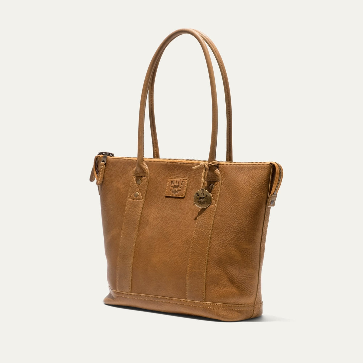 Tan pebbled leather zip tote, three-quarter angle view showing the side gusset and zipper