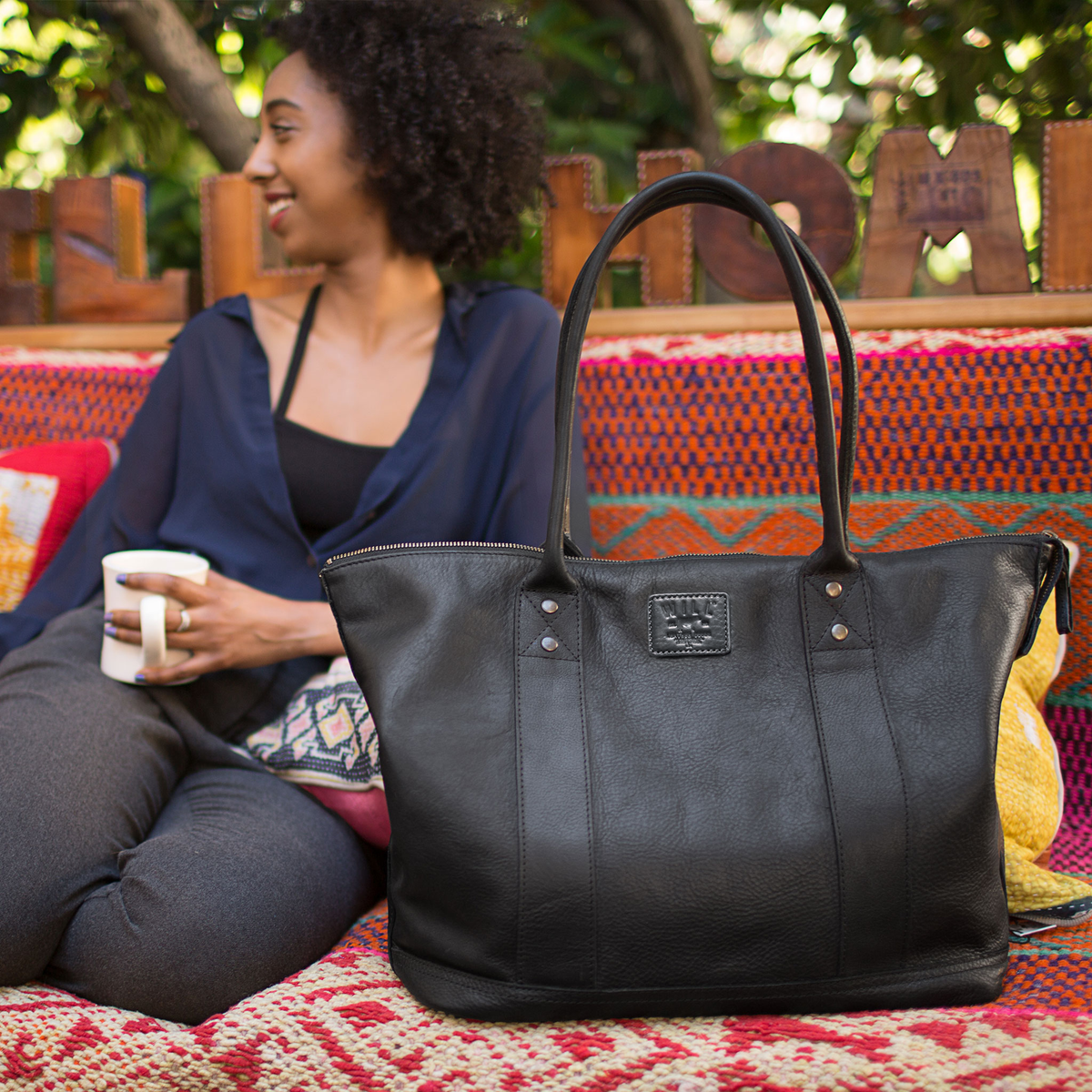 Lifestyle photo of a woman relaxing outdoors with the black leather tote resting beside her