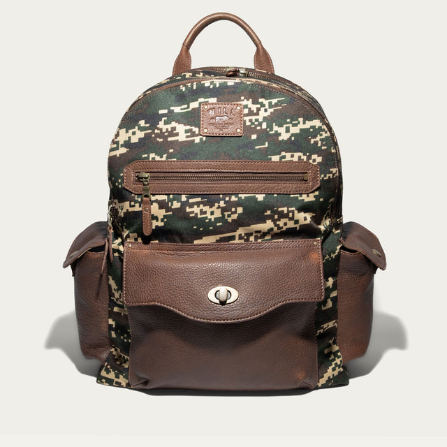 Will Leather Goods Canvas + Leather Backpack in green digital camo canvas with brown leather trim, front view showing the zip front pocket, flap pocket with turn-lock closure, and two side pockets, on a white background.