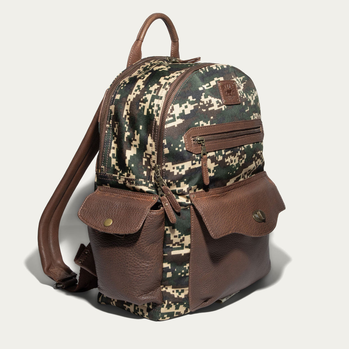 Side angle of the green digital camo Canvas + Leather Backpack showing the brown leather top handle, side pockets, and adjustable straps.