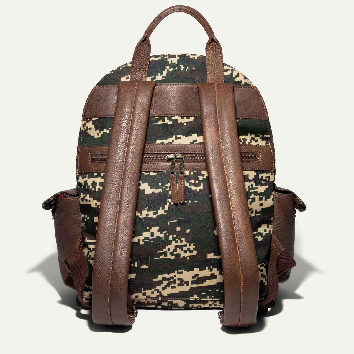 Back view of the green digital camo Canvas + Leather Backpack showing the brown leather top handle, padded shoulder straps, and rear zip pocket.
