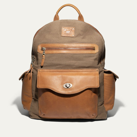 Will Leather Goods Canvas + Leather Backpack in olive canvas with tan leather trim, front view showing the zip front pocket, flap pocket with turn-lock closure, and two side pockets, on a white background.