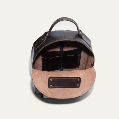 Dark brown leather backpack open and packed with a water bottle, red wallet, book, and sneakers inside the main compartment.