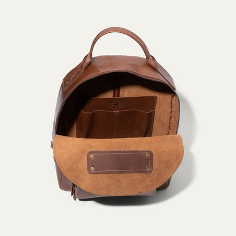 Interior view of the tan leather backpack open, showing the suede-lined main compartment and an interior slip pocket.