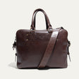 Dark brown leather briefcase, front view, with rolled top handles, adjustable shoulder strap, and embossed WILL Leather Goods logo patch