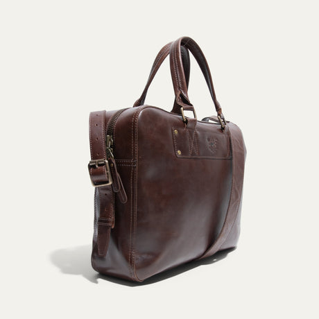 Angled side view of the dark brown leather briefcase showing the rolled handles, shoulder strap, and WILL Leather Goods logo patch