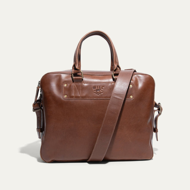 Tan leather briefcase, front view, with rolled top handles, adjustable shoulder strap, and embossed WILL Leather Goods logo patch