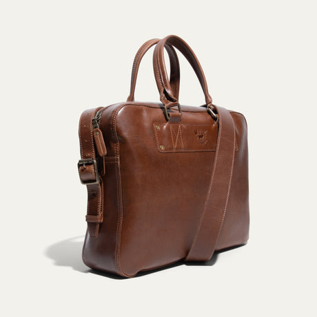 Angled side view of the tan leather briefcase showing the rolled handles, shoulder strap, and WILL Leather Goods logo patch
