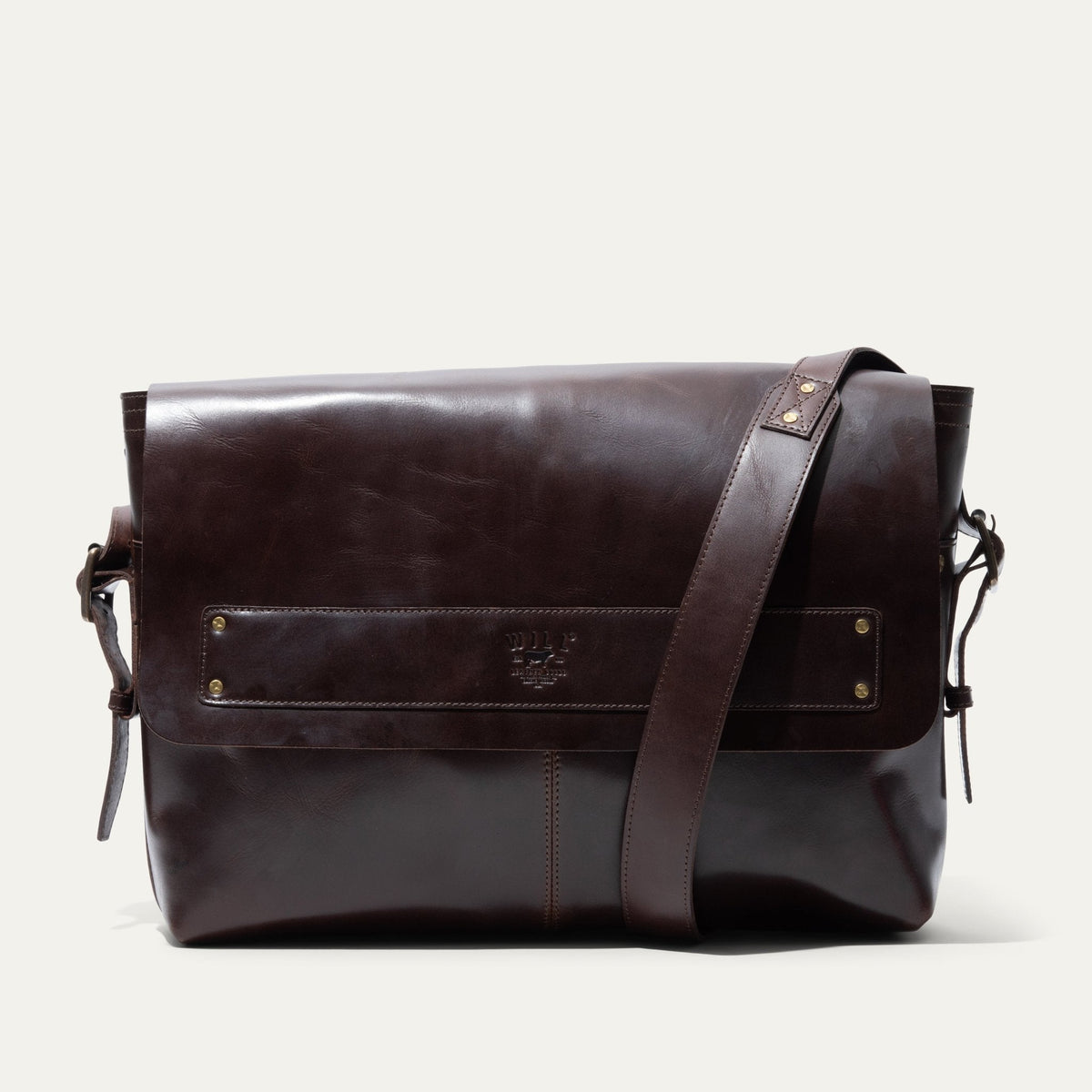 Will Leather Goods Field Messenger bag in dark brown leather, three-quarter angled view showing the buckled shoulder strap and embossed WILL logo strip.