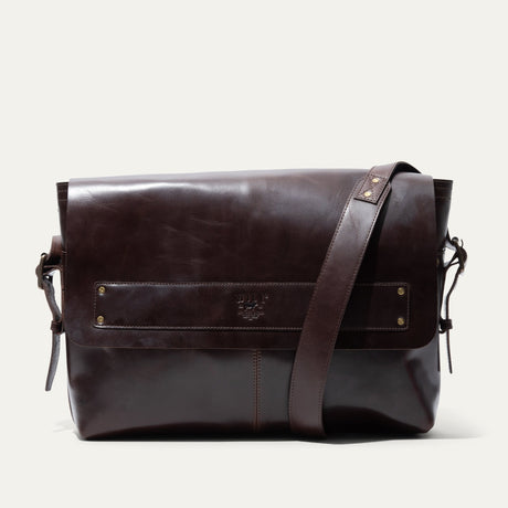 Will Leather Goods Field Messenger bag in dark brown leather, three-quarter angled view showing the buckled shoulder strap and embossed WILL logo strip.