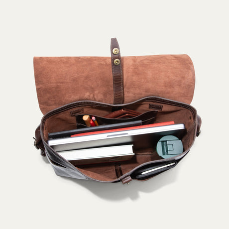 Will Leather Goods Field Messenger bag in dark brown leather, opened flat and packed with a laptop, notebooks, pens, a wallet, and a round travel case inside the suede-lined interior.