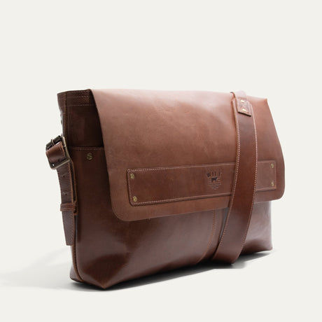 Will Leather Goods Field Messenger bag in tan leather, three-quarter angled view showing the buckled shoulder strap and embossed WILL logo strip.