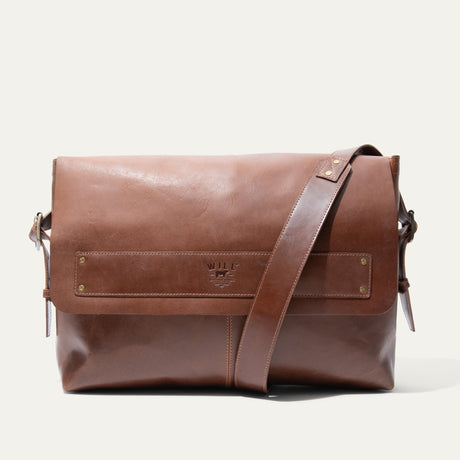 Will Leather Goods Field Messenger bag in tan leather, front view standing with the flap closed, shoulder strap draped to the side, and embossed WILL logo strip across the flap, on a white background.