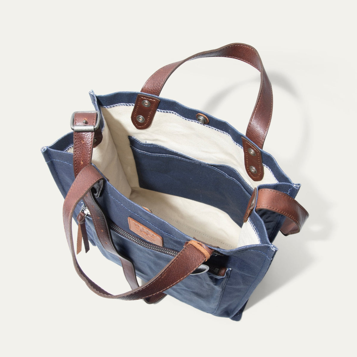 Overhead view looking down into the empty navy tote, showing the cream canvas interior lining, open slip pocket, and leather handle attachment points