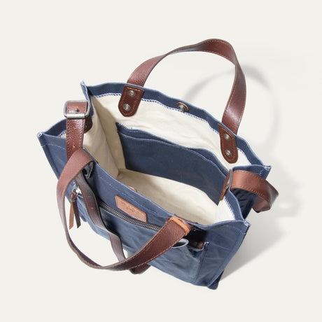 Overhead view looking down into the empty navy tote, showing the cream canvas interior lining, open slip pocket, and leather handle attachment points