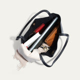 Overhead view into the open black Workshop Tote, showing the suede-lined interior packed with a laptop, notebooks, a red zip pouch, a tan zip pouch, keys, and a cream scarf.