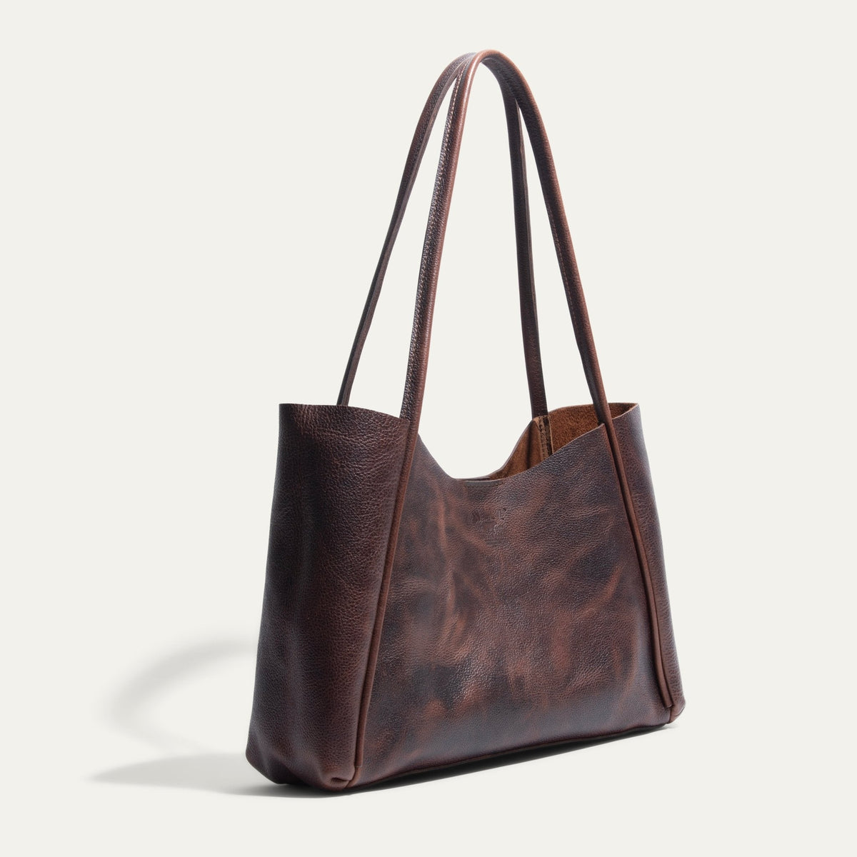 Side angle of the brown Workshop Tote showing its pebbled leather texture, tall curved handles, and embossed Will Leather Goods logo.