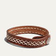 Will Leather Goods Cross Stitch Cuff in brown leather, looped into an oval to show the cream cross-stitch band running around the strap and the antique brass snap closure, on a white background.