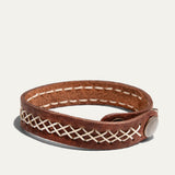 Will Leather Goods Cross Stitch Cuff in brown leather, looped into an oval to show the cream cross-stitch band running around the strap and the antique brass snap closure, on a white background.