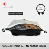 A white Compak Large with Divider holding black knitwear below the divider and tan and grey clothing above it, labelled Now With Divider, with a New Arrival badge and a strip reading Featured in Conde Nast Traveler, Tatler, GQ, WIRED and GLAMOUR