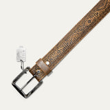 Close-up diagonal view of the Freedom Wild One belt's antique silver buckle and keeper loop with a stamped cow-head rivet, tooled tan leather strap, and the metal Will Leather Goods hang tag attached by a ball chain.