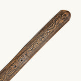 Close-up angled view of the rounded belt tip on the Freedom Wild One belt, showing the tooled southwestern geometric pattern and stamped rivets along the tan leather strap.