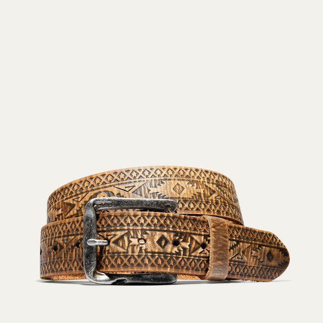 Will Leather Goods Freedom Wild One belt in distressed tan leather with an all-over tooled southwestern geometric pattern, coiled to show the antique silver buckle, on a white background.