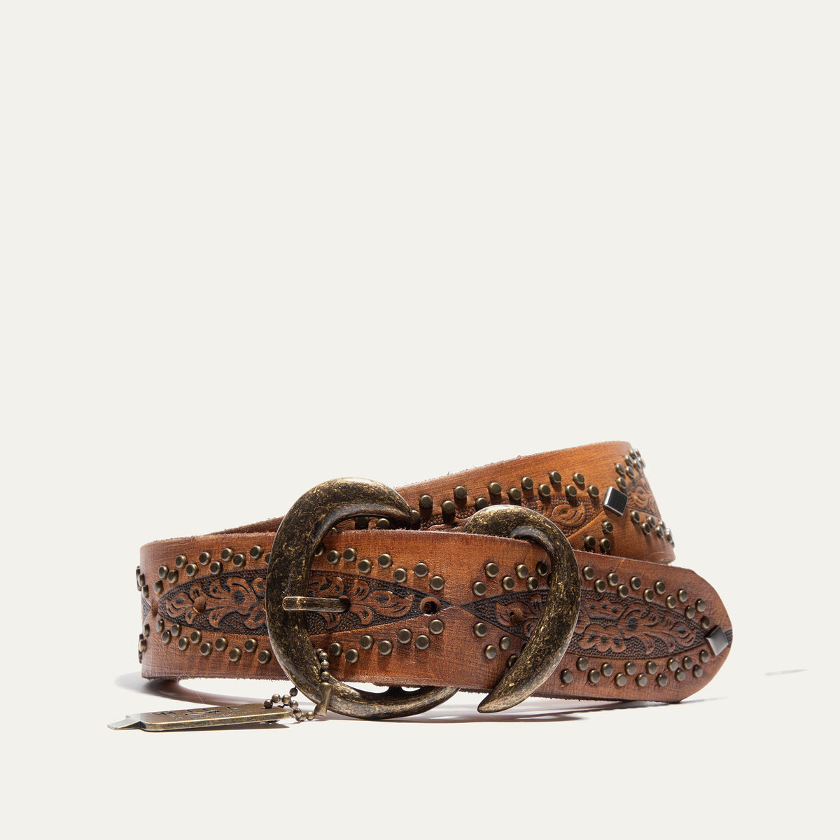 Will Leather Goods Baez Wild Ones Belt coiled on a white background, tan leather with tooled floral tabs, brass studs, diamond conchos, and an antiqued brass double-prong buckle with a Will Leather Goods hang tag.