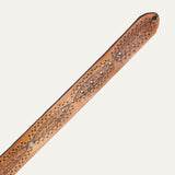 Close-up of the belt's rounded tip end, showing tooled floral tabs, brass stud trim, and diamond conchos on tan leather with visible buckle holes.