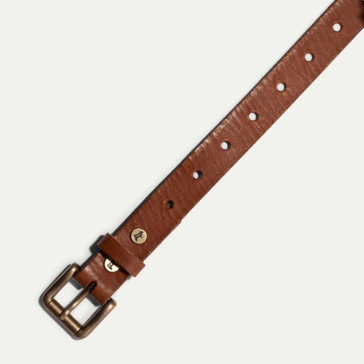 Close-up diagonal view of the cognac leather Bridal Belt showing the sizing holes, brass roller buckle, and embossed cow-head rivet on the keeper loop.