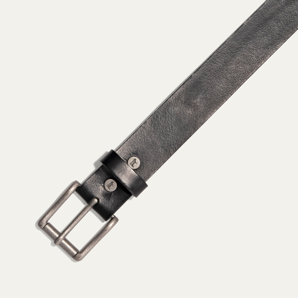 Close-up diagonal view of the black leather Bridal Belt's antique silver roller buckle, sizing holes, and embossed cow-head rivets on the keeper loop.