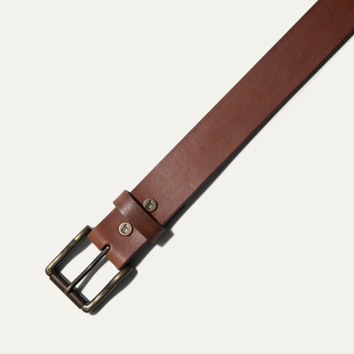 Close-up of the cognac leather belt's antique brass buckle and keeper loop with cattle snaps