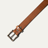 Close-up of the tan leather belt's antique brass buckle and keeper loop with cattle snaps