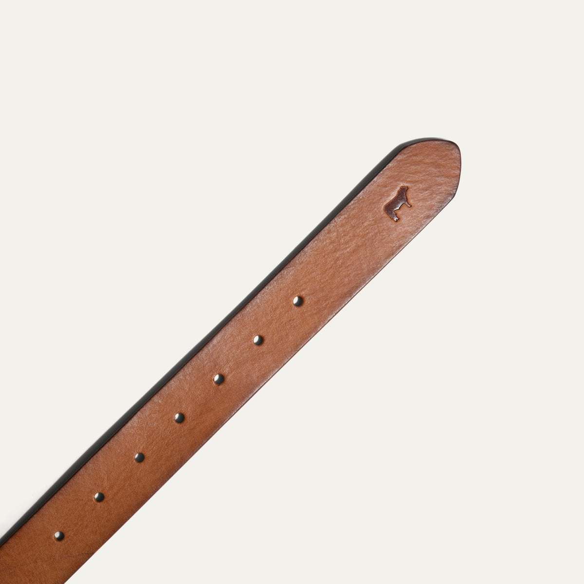 Close-up of the tan leather belt's tip, showing the embossed cattle logo and adjustment holes