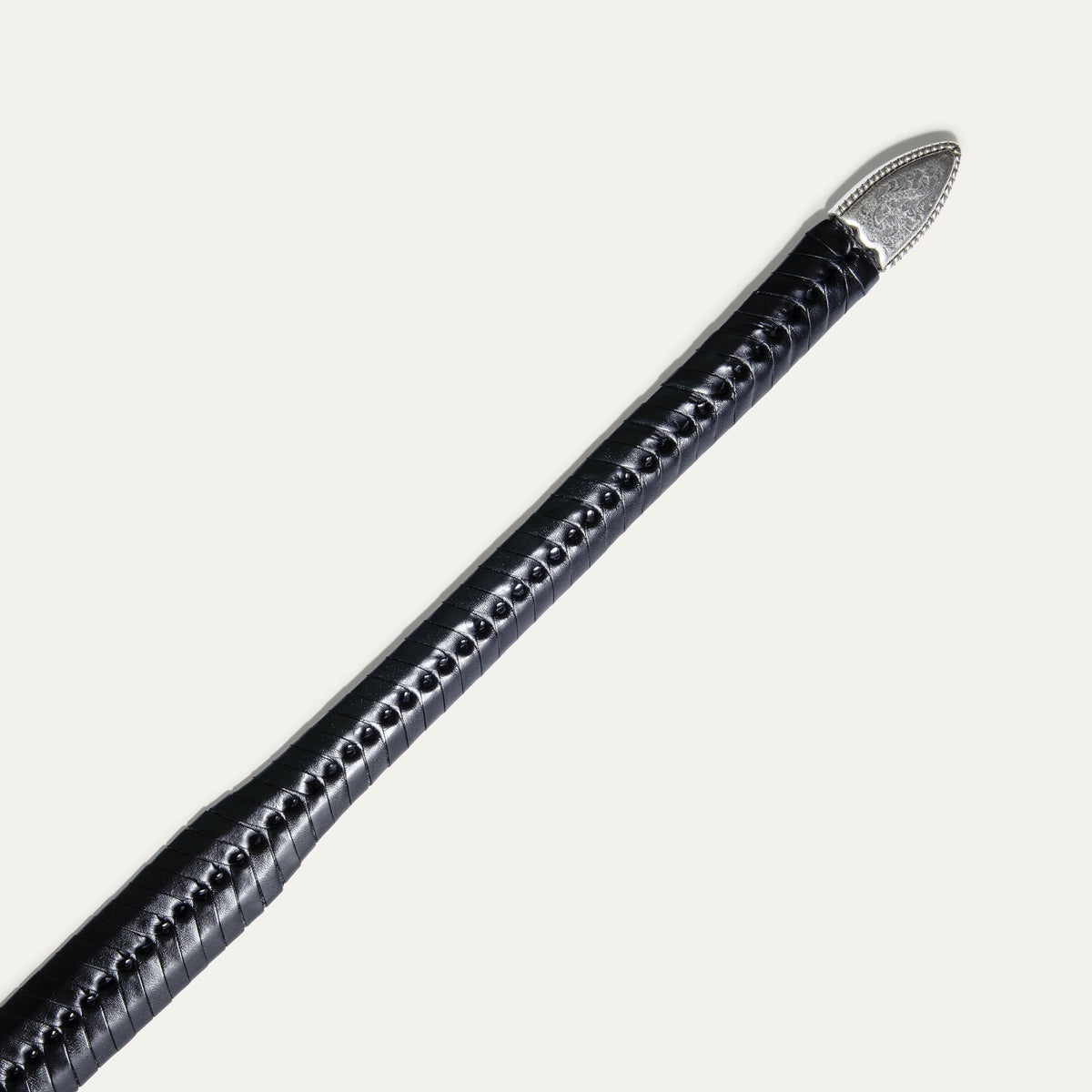 Close-up of the black tapered lace belt strap tip end with the engraved silver metal cap.