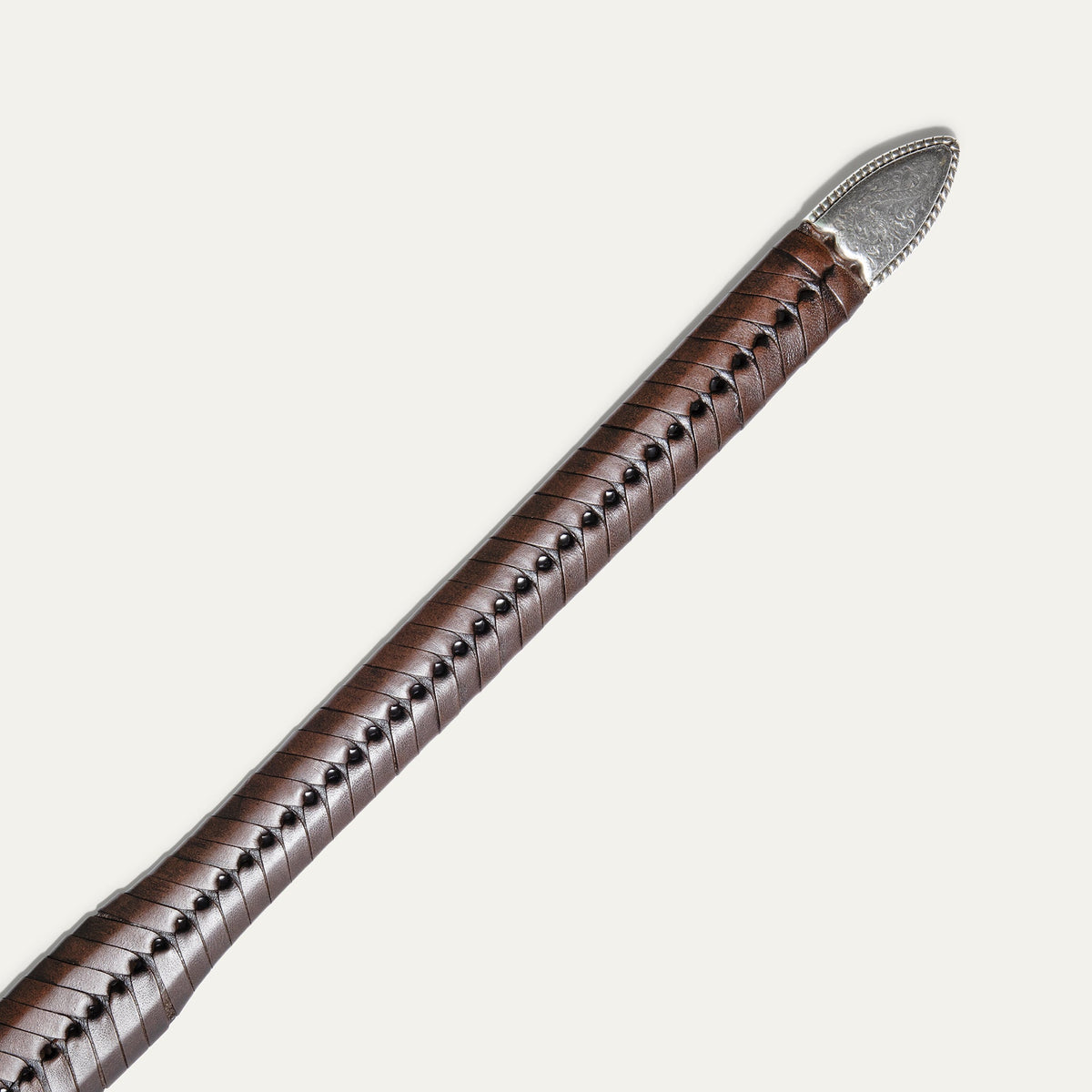 Close-up of the cognac brown tapered lace belt strap tip end with the engraved silver metal cap.