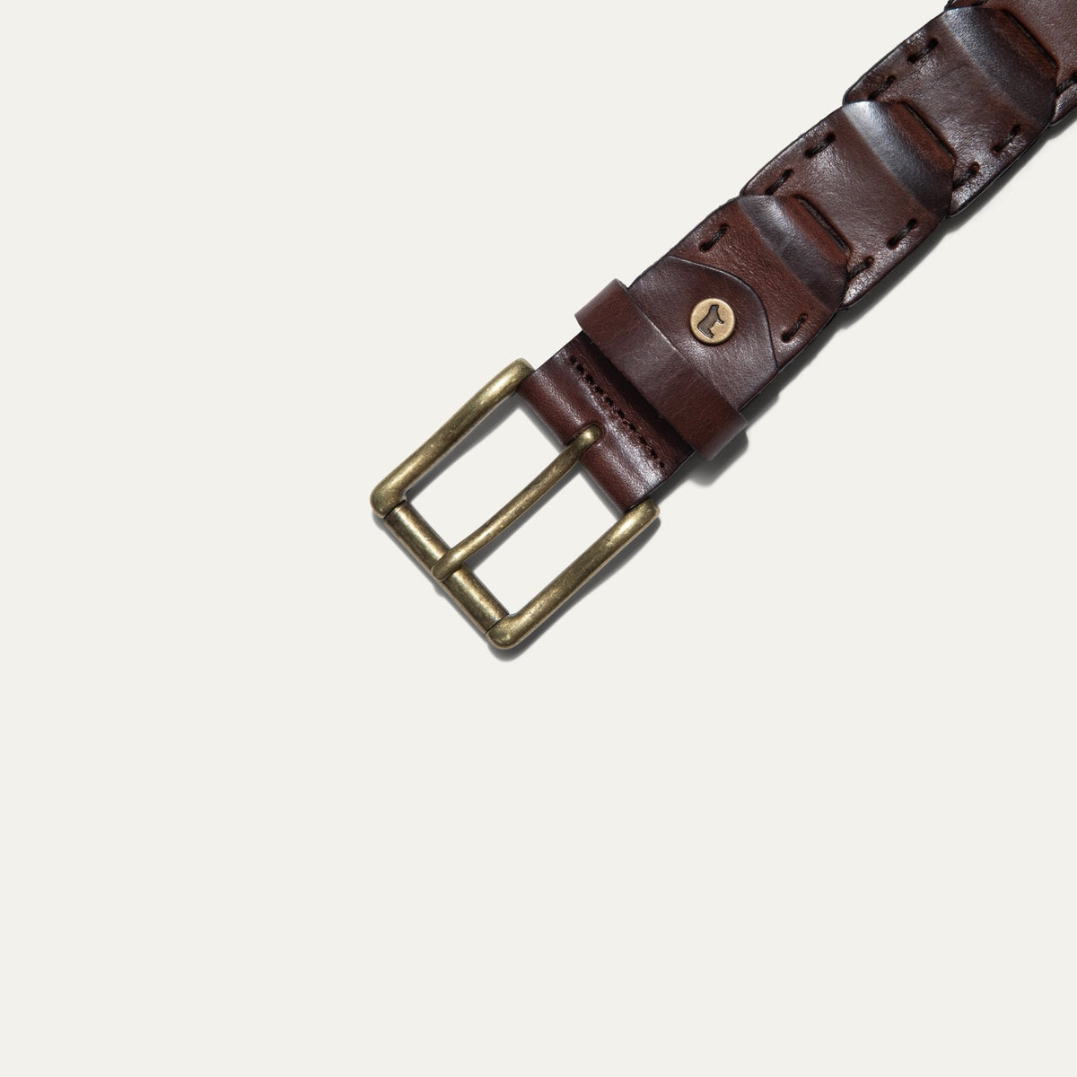 Close-up overhead view of the brown leather Hand Laced Link Belt showing the hand-laced stitching between rectangular link panels and the antique brass roller buckle with embossed cow-head rivet.