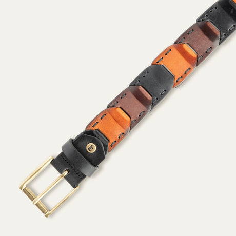 Close-up overhead view of the tri-color black, brown, and cognac Hand Laced Link Belt showing the hand-laced link panels and antique brass roller buckle with embossed cow-head rivet.