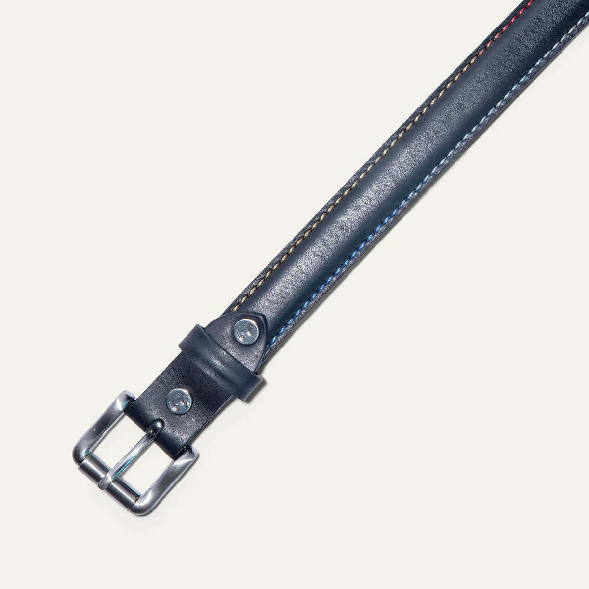 Close-up of the Rainbow Stitched Belt buckle in navy leather, showing the brushed nickel roller buckle and multicolor edge stitching.