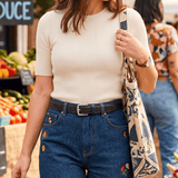 Lifestyle photo of a woman wearing the Rainbow Stitched Belt in navy leather with a nickel buckle over dark denim jeans at an outdoor market.