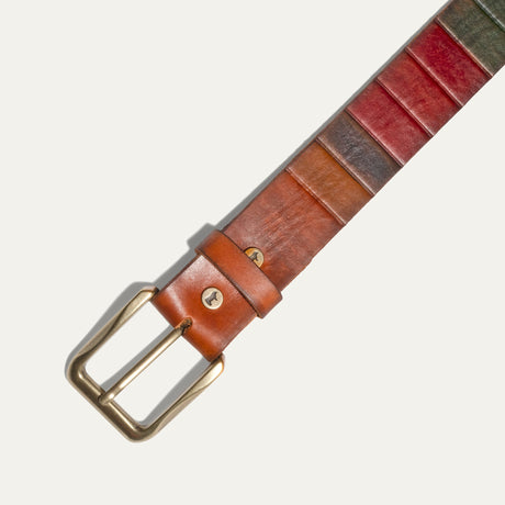 Close-up of the Hand Painted Color Block Belt's brass roller buckle and keeper loop, showing the embossed Will Leather Goods cattle-brand snap stud and hand-painted panels in tan, red, navy, and olive.