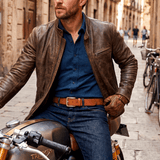 Lifestyle photo of a man in a brown leather jacket and jeans wearing the cognac Razor Cut Belt with a brass buckle, straddling a cafe-racer motorcycle.