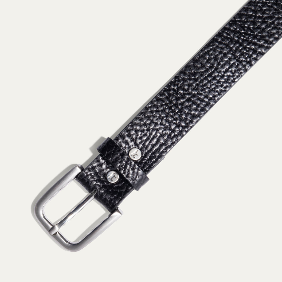 Close-up of the Shrunken American Bison Belt buckle in black pebbled bison leather, showing the brushed nickel buckle and embossed WILL Leather Goods dog logo rivets.