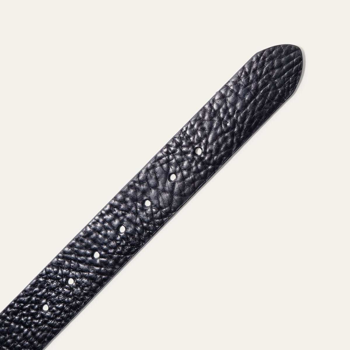 Close-up of the Shrunken American Bison Belt strap in black pebbled bison leather, showing the textured grain and row of adjustment holes near the rounded tip.