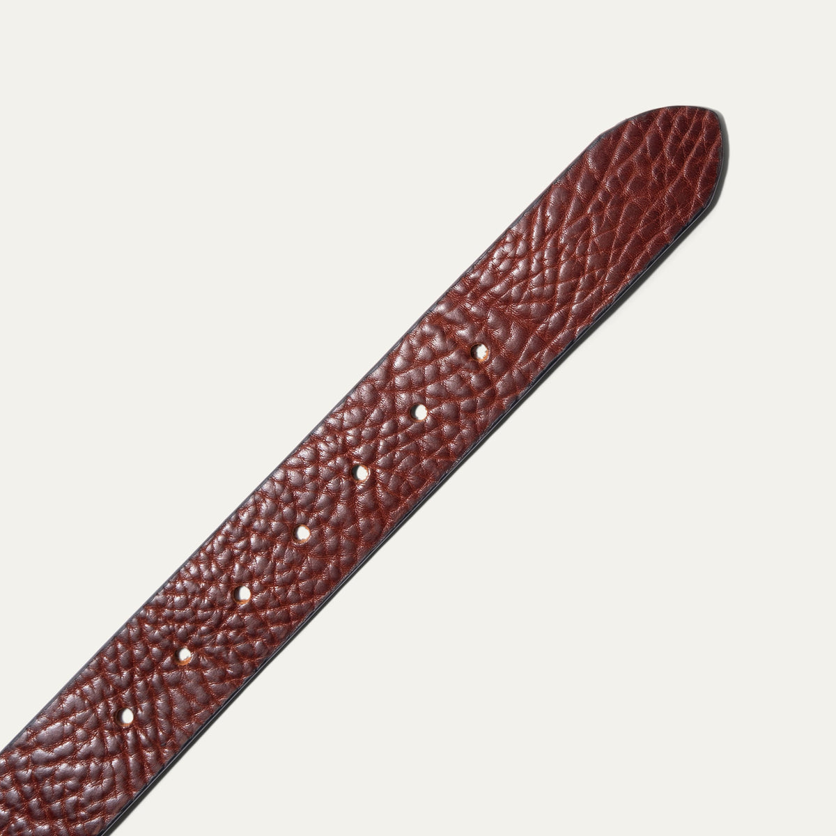Close-up of the Shrunken American Bison Belt strap in brown pebbled bison leather, showing the textured grain and row of adjustment holes near the rounded tip.