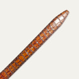 Close-up of the cognac Croco Belt's tapered tip end, showing the crocodile-embossed grain, edge stitching, and adjustment holes.
